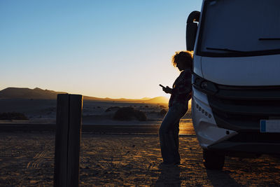 Rear view of woman standing on beach against clear sky during sunset