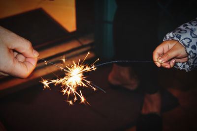 Cropped hands holding sparklers at night