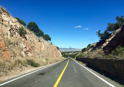 Empty road by trees against blue sky