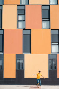 Full body of young guy in casual wear riding on unicycle on modern urban street with colorful building