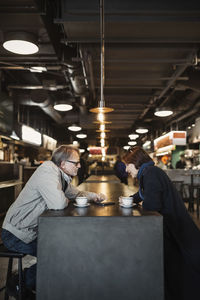 Side view of senior couple using mobile phone while having coffee at cafeteria