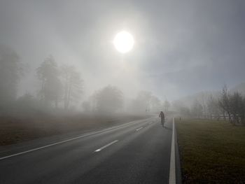 Country road amidst trees against sky during foggy weather