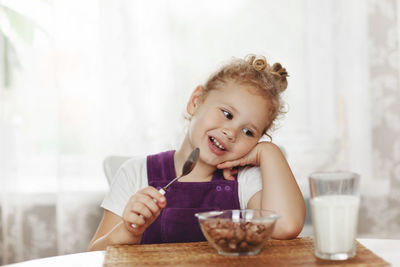 Cute little baby girl having breakfast cereal with milk in the kitchen. the girl holds a spoon 