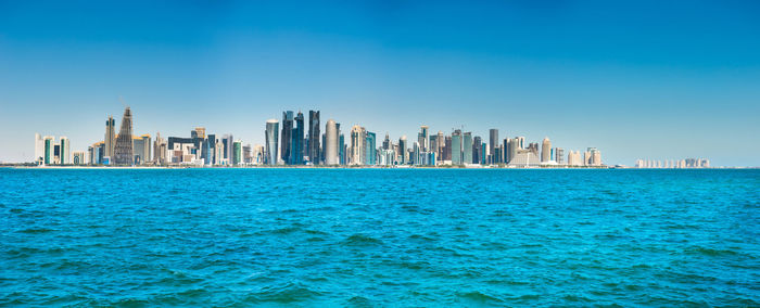 Sea by buildings in city against blue sky