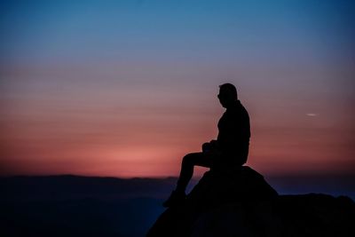 Silhouette man sitting on rock against sky during sunset