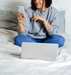 Midsection of woman using smart phone while sitting on bed