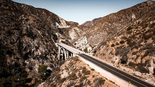 Road leading towards rocky mountains against clear sky