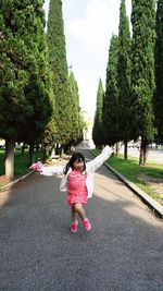 Full length of cheerful girl standing with arms outstretched amidst trees