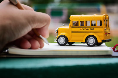 Cropped hand writing in paper by toy school bus
