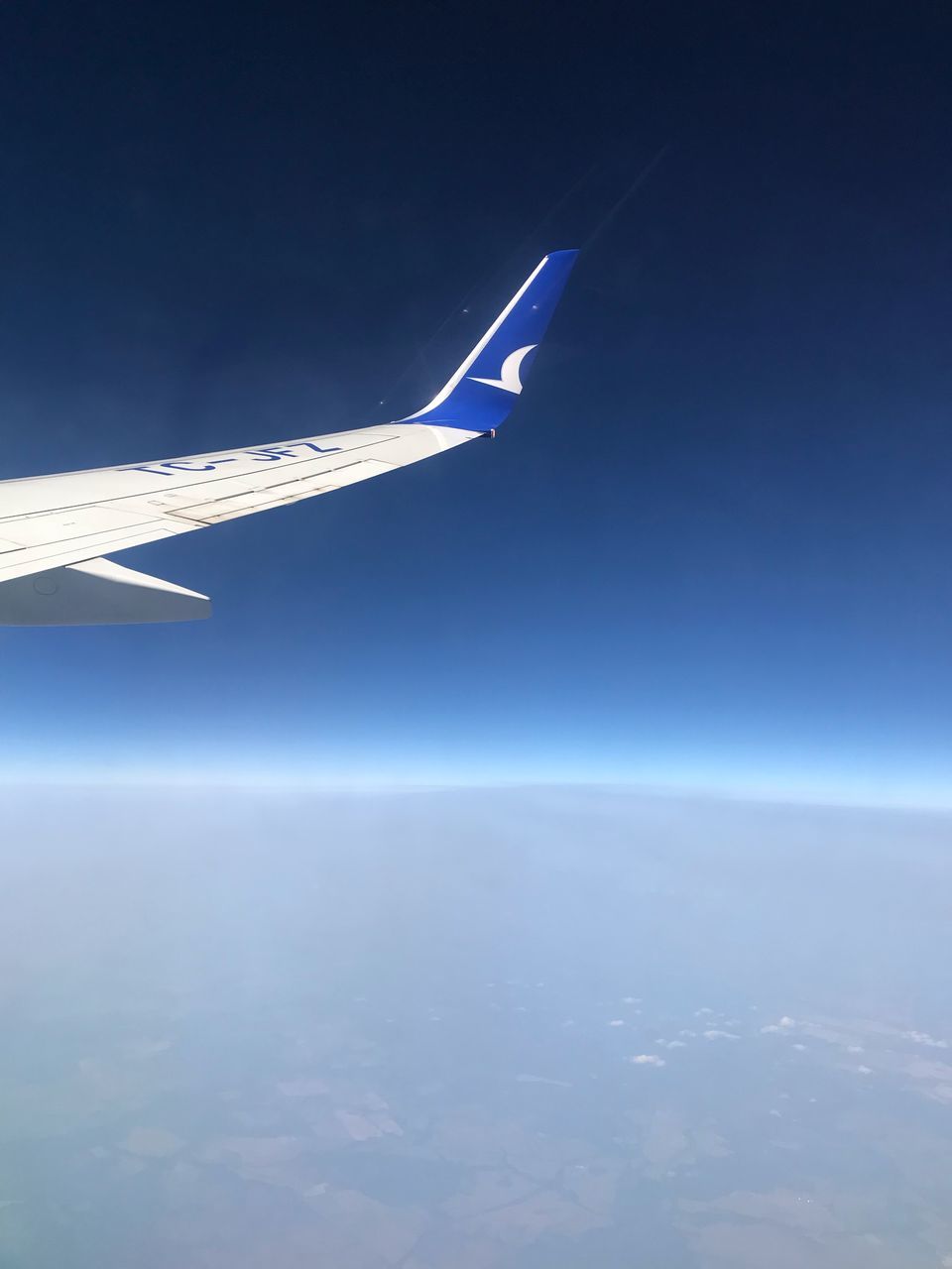 AERIAL VIEW OF AIRPLANE FLYING OVER SEA AGAINST BLUE SKY