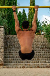 Rear view of shirtless man with arms raised