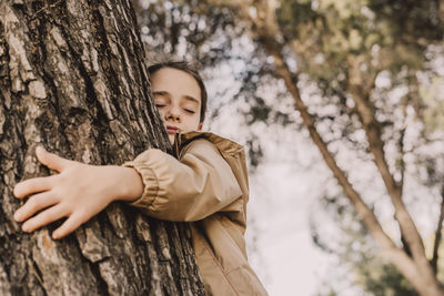 Cute girl with eyes closed hugging tree at park