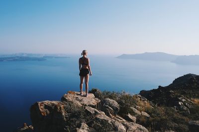 Woman standing on rock by sea against clear sky