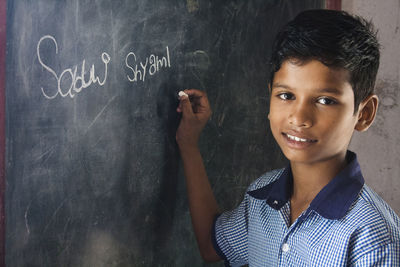 Portrait of boy writing on blackboard