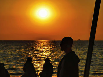 Silhouette people looking at sea against sky during sunset