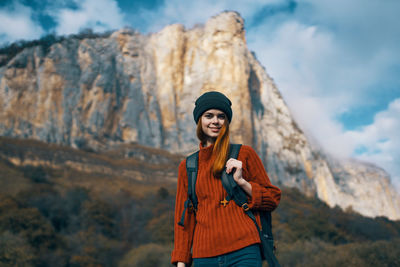 Portrait of smiling young woman standing against mountains