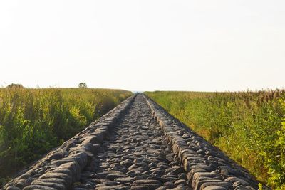 Road passing through field against clear sky