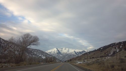 Road by trees against sky during winter