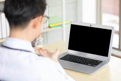 Rear view of man using laptop on table