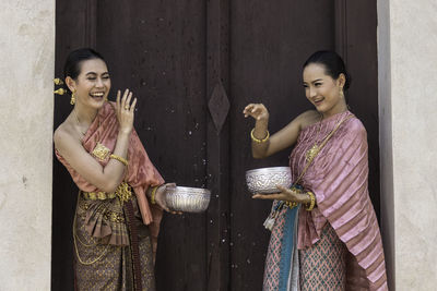 Smiling women wearing traditional clothing holding bowls while standing by wall