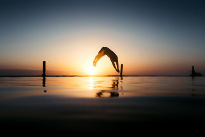 Low section of man jumping against sky during sunset