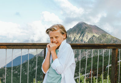 Portrait of boy standing by railing against mountains and sky