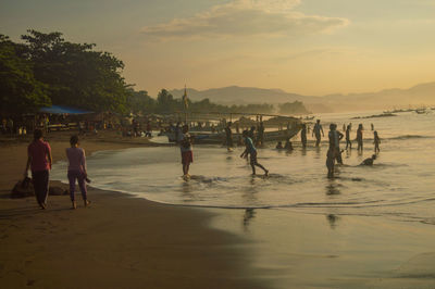 People enjoying on beach against sky during sunset