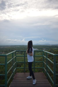 Rear view of woman standing on railing against sky