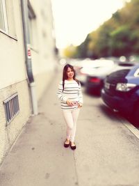 Tilt-shift image of young woman standing by car on sidewalk
