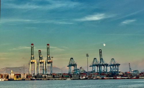 Cranes at harbor against sky