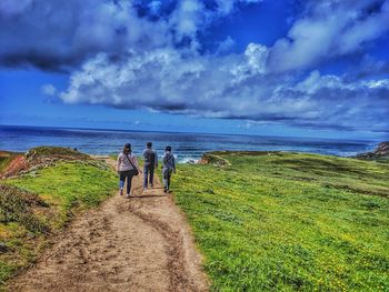 Rear view of people walking on beach against sky