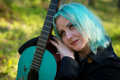 Hipster young woman with turquoise guitar looking away in forest