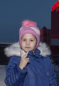 Portrait of cute girl showing peace sign while standing against clear sky