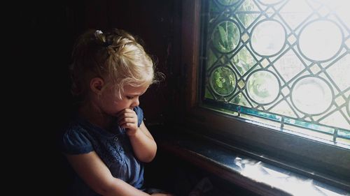 Sad girl sitting by window at home