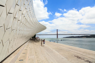 People on bridge over sea against cloudy sky