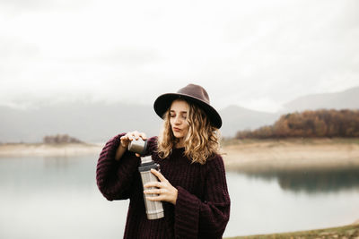 Young woman standing by lake against sky during winter