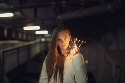 Portrait of young woman holding illuminated string light at night