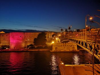 Illuminated bridge over river against sky in city at night