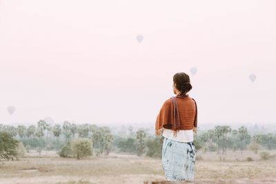Rear view of woman standing on field against sky