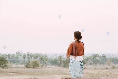 Rear view of woman standing on field against sky