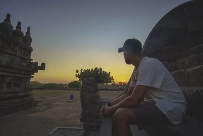 Side view of a man sitting against sky during sunset