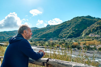 Side view of a happy thoughtful bearded man contemplating mountain nature with cloudy sky. 