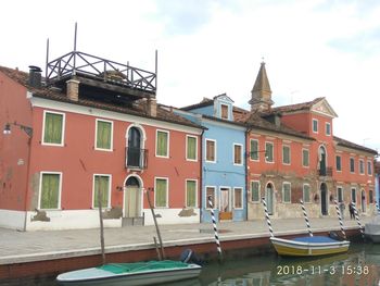 Boats moored in canal by buildings against sky