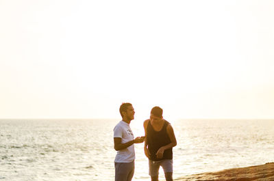 Male friends standing at beach during sunrise