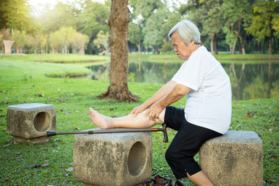 Side view of man sitting on grassland against trees