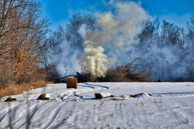 Smoke emitting from land against sky during winter