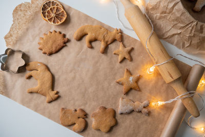 A frame of ginger cookies of different shapes on parchment, a rolling pin on the table and garlands