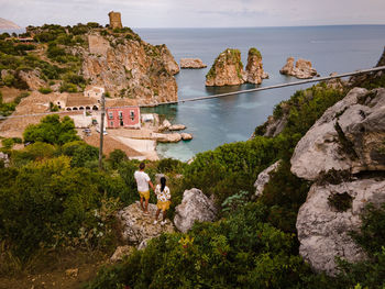 People on rock by sea against sky