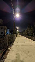 Illuminated street amidst buildings against sky at night