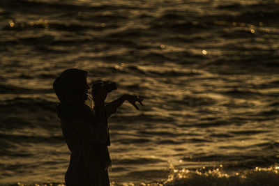 Silhouette woman photographing on beach during sunset